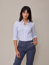 Camisa celeste a rayas verticales blancas, de manga 3/4 con puños arremangados y cuello clásico.