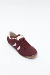 Zapatilla urbana de perfil bajo con diseño retro, confeccionada en poliuretano con detalles en textura tipo gamuza. Presenta puntera redondeada, cordones clásicos y suela de goma color caramelo.