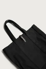 Bolso tipo shopper de algodón color negro, con asas superiores y tira de cuero con botón metálico para el cierre. Diseño amplio y versátil para uso diario.