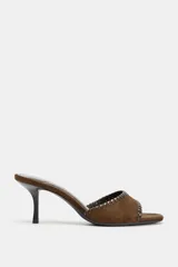 Sandalia tipo mule de gamuza color marrón, con tira delantera decorada con pespuntes en contraste, tacón fino y punta cuadrada.