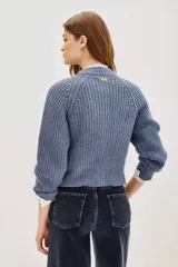 Cardigan de punto acanalado color azul grisáceo, de corte cropped y abotonadura frontal. Presenta apliques florales bordados con cuentas y lentejuelas en tonos azules y verdes en la parte delantera.