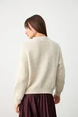 Sweater de punto color crudo, con cuello redondo y diseño de bordado floral en el frente. Presenta mangas largas con puños acanalados y un corte holgado.