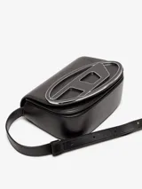 Bandolera Diesel modelo 1DR M, color blanco, confeccionada en cuero vacuno liso. Presenta una solapa con una placa metálica esmaltada del logo D ovalado. Incluye correa ajustable para llevar al hombro o cruzada, compartimento principal amplio y dos secciones planas internas.