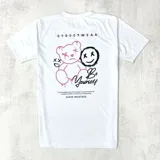Remera blanca de manga corta con estampado en la espalda que incluye un oso de peluche, una cara sonriente y la frase "Be Yourself".