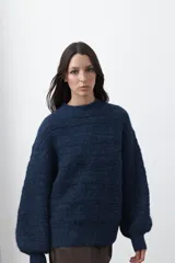 Sweater de punto color marrón chocolate, con cuello redondo, mangas largas abullonadas y puños ajustados. Presenta un diseño de textura acanalada horizontal y silueta relajada.