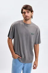 Remera de manga corta con efecto lavado, color gris oscuro, con cuello redondo y un pequeño parche rectangular con texto en el pecho.