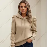 Buzo tipo hoodie color beige, con capucha y cordones ajustables. Presenta un diseño distintivo de mangas princesa con frunces en los hombros y puños elásticos, confeccionado en una mezcla de poliéster y elastano.