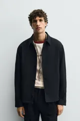 Sobrecamisa negra de corte regular, confeccionada en tejido compacto. Presenta cuello solapa, manga larga con puños abotonados y bolsillos de vivo en la cadera. Cierre frontal con botonadura.