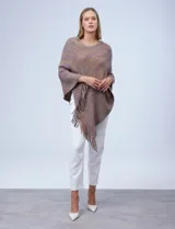 Poncho tejido en hilo soft, con efecto jaspeado multicolor (predominantemente tonos oscuros como azul marino, negro, y toques de violeta y dorado/lurex). Presenta un diseño asimétrico y flecos largos en los bordes.