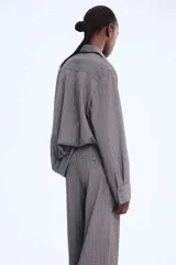 Pantalón sastrero de corte ancho y tiro alto, color gris oscuro con finas rayas verticales blancas (pinstripe). Presenta pliegues frontales (pinzas) y pretina con cierre oculto.