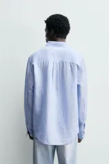 Camisa regular fit de manga larga con diseño a rayas verticales celestes y blancas. Cuenta con cuello abotonado, bolsillo de parche en el pecho y cierre frontal con botones.