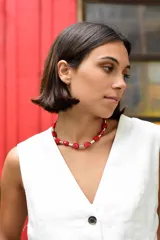 Collar tipo gargantilla compuesto por cuentas de piedra roja en forma irregular intercaladas con cilindros metálicos plateados. Cuenta con cadena de acero quirúrgico para ajustar el largo.