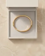 Pulsera esclava de acero con baño de oro, compuesta por una hilera de circonias engarzadas en bisel.