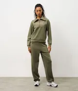 Buzo deportivo de corte oversized en color verde oliva, confeccionado en tejido modal con mezcla de poliéster y elastano. Presenta cuello alto con cierre frontal de cremallera y paneles frontales con textura acanalada. Incluye mangas largas con puños elásticos ajustados.