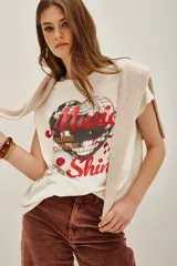 Remera de algodón color crema con estampa frontal de una bola de espejos en forma de corazón y texto en tonos rojos y negros.