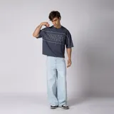 Remera gris oscuro de corte boxy, manga corta amplia, con cuello redondo y diseño gráfico frontal con la palabra "CONCEPTO" delineada en blanco dentro de un panel horizontal.