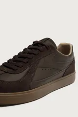 Zapatilla deportiva estilo retro en color marrón, confeccionada con una combinación de piezas de cuero sintético y gamuza, con suela de goma a tono.