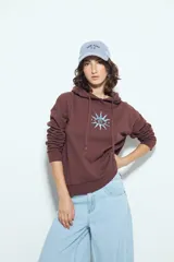 Canguro negro de calce relajado con capucha y cordones ajustables. Presenta un estampado gráfico frontal de un ojo con rayos de sol y la frase "STAY WEIRD".