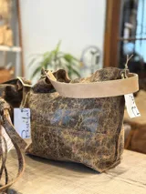 Cartera tipo bolso de hombro con diseño de estampado animal print de leopardo. Cuenta con una correa fija de longitud media y herrajes metálicos en tono bronce envejecido que conectan la correa con el cuerpo del bolso.