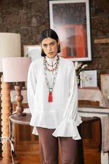 Blusa blanca de textura arrugada, con cuello alto, abertura frontal tipo gota y mangas largas acampanadas con detalle de frunces.
