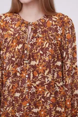 Blusa marrón con estampado de flores color naranja y blanco, con cuello redondo con abertura y mangas largas abullonadas.