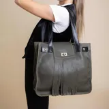 Cartera tipo tote de cuero color verde oliva, con diseño estructurado, flecos frontales y cierre metálico giratorio. Cuenta con correas de hombro en cuero negro y detalles de remaches dorados.