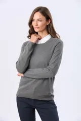 Buzo tejido en hilo de algodón color beige, con cuello redondo y manga larga. Presenta un corte clásico y un pequeño detalle metálico en la parte inferior izquierda.