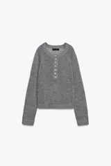 Jersey de punto color gris, con cuello redondo y abertura frontal con botones. Presenta mangas largas raglán y puños y bajo acanalados.