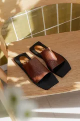 Sandalias planas con punta cuadrada, base negra y capellada de cuero marrón con textura trenzada.