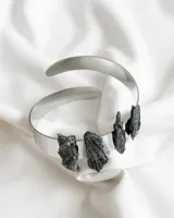 Brazalete rígido plateado con piedras negras irregulares incrustadas.