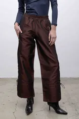 Pantalón de tafeta tornasolada color borgoña, de corte recto y tiro alto, con cintura elastizada, bolsillos frontales con cierre y cordones ajustables en las pantorrillas para fruncir el bajo.