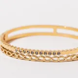 Pulsera rígida dorada con doble banda, una con diseño calado y otra con incrustaciones de strass.