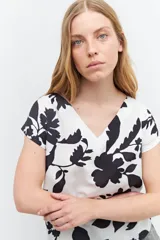 Blusa blanca con estampado de flores negras, escote en V y mangas cortas.