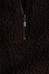 Buzo de sherpa con textura de peluche, cuello elevado y medio cierre frontal. Presenta hombros caídos, mangas largas y bolsillos laterales insertados.