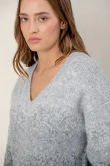 Sweater de punto con escote en V, diseño de mangas largas y efecto degradado que transiciona de un tono crema en la parte superior a un tono beige en la parte inferior.