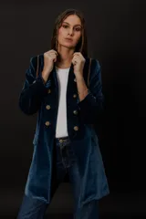 Chaqueta azul de terciopelo con corte levita, cuello mao y doble botonadura dorada.