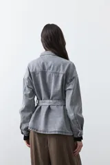 Sobrecamisa de jean color negro con silueta relajada, cuello camisero, cierre frontal con botones metálicos, bolsillos frontales y cinturón ajustable en la cintura.
