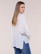 Camisa blanca de silueta holgada y textura liviana, con cuello camisero clásico, abotonadura frontal con botones en contraste y doble bolsillo de parche en el frente. Cuenta con mangas de corte dolman de largo tres cuartos con puño amplio y ruedo recto con aberturas laterales.