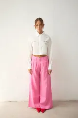 Camisa blanca de popelina de algodón, de corte cropped, con cuello clásico y cierre frontal de botones. Presenta bordados rojos en el frente con las frases "el poder" y "DEL AMOR", y un bolsillo de parche en el lado derecho.