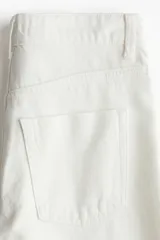 Jean de tiro alto con corte wide leg, confeccionado en denim rígido de color blanco. Presenta diseño clásico de cinco bolsillos, cierre frontal con botón y ruedo con terminación desflecada.