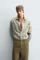 Camisa de corte relajado confeccionada en tejido fluido con estampado geométrico en tonos azules y ocres. Presenta cuello solapa, cierre frontal de botones y manga larga con puños abotonados.