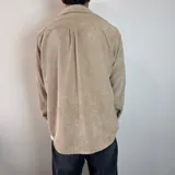 Sobrecamisa de pana negra con cierre frontal de botones, cuello clásico, mangas largas con puños abotonados y un bolsillo en el pecho.