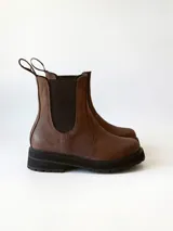 Bota tipo Chelsea de cuero color chocolate, con paneles elásticos laterales, tirador trasero y suela track negra de goma.