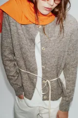 Chaqueta de punto de cuello redondo y manga larga, con diseño combinado que incluye una capa interior en tono crudo. Presenta cierre frontal con botones y puños acanalados.