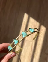 Brazalete rígido dorado con tres piedras turquesas irregulares engarzadas.