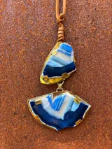 Collar largo de tiento de cuero marrón con dije colgante doble de piedras ágatas en tonos marrones y naranjas, engarzadas en metal dorado.