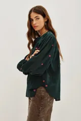 Camisa de algodón color crudo con bordados florales pequeños en azul marino. Presenta mangas largas abullonadas, cuello redondo y una abertura frontal con botones y detalles de encaje calado en la pechera y hombros.