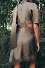 Vestido midi satinado de cuello subido y manga corta tipo capa. Presenta aberturas laterales con aplicación de encaje a tono y bajo asimétrico con detalle de encaje. Incluye un pañuelo integrado en el mismo tejido y cierre posterior con botones forrados.