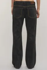 Jeans de denim negro de tiro medio y corte bootcut, con tachas metálicas doradas a lo largo de los laterales y en los bolsillos delanteros.