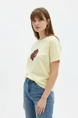 Remera cropped de algodón color amarillo claro con diseño estampado de una flor en el pecho, cuello redondo y mangas cortas de corte holgado.